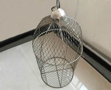 A bird cage made up of stainless steel ferrule rope mesh is on the floor.
